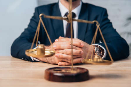 selective focus of golden scales near lawyer in suit with clenched hands