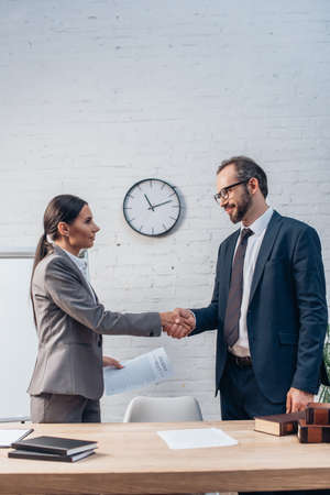 lawyers in formal wear shaking hands near documents in officeの写真素材
