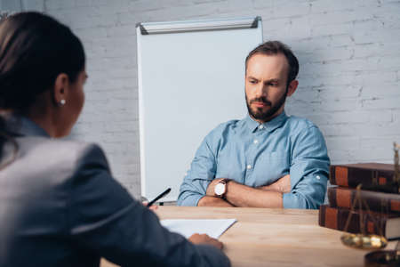 selective focus of displeased man sitting with crossed arms near lawyer and books on tableの写真素材