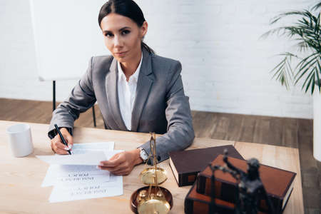 selective focus of brunette lawyer in formal wear holding pen near insurance policy documents and...
