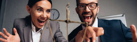 panoramic shot of excited businessman and businesswoman in formal wear touching scales