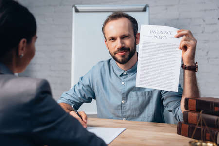 selective focus of bearded man holding insurance policy agreement and pen near brunette lawyerの写真素材