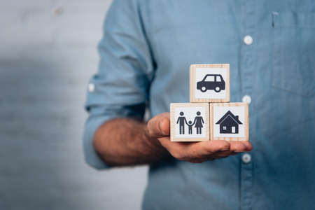cropped view of man holding wooden cubes with car, family and house in handの写真素材
