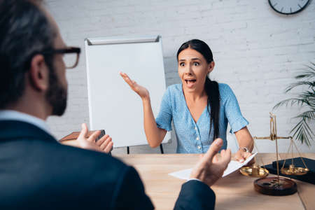 selective focus of brunette client screaming and gesturing while holding contract near lawyer in...