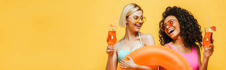 young interracial women in summer outfit holding swim ring and cocktail glasses while looking at...