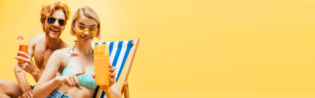 panoramic concept of blonde woman pointing with finger at orange juice near man with cocktail glass...