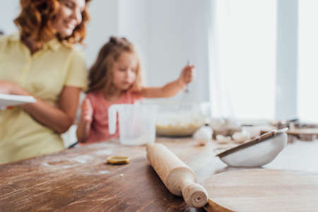 selective focus of chopping board, rolling pin and sieve near mother and daughter cooking in kitchenの写真素材