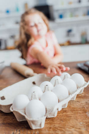 selective focus of child taking chicken egg from tray on kitchen tableの写真素材