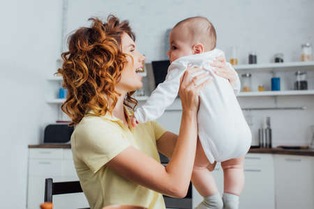 young, curly mother holding infant boy in kitchenの写真素材