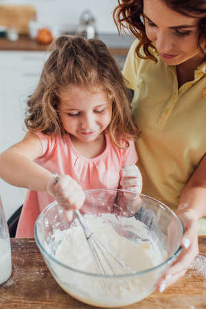high angle view of mother touching glass bowl while daughter kneading dough with whiskの写真素材