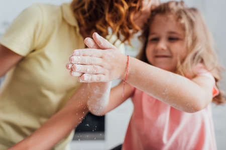 cropped view of girl with hands in flour near mother, selective focusの写真素材