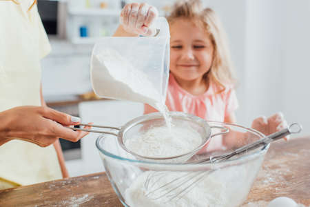 partial view of woman holding sieve while daughter adding flower into glass bowl, selective focusの写真素材