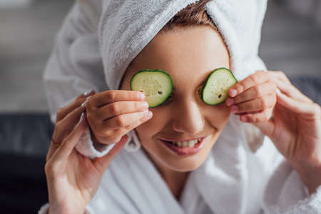 cropped view of child applying fresh cucumber slices on eyes of mother, selective focusの写真素材
