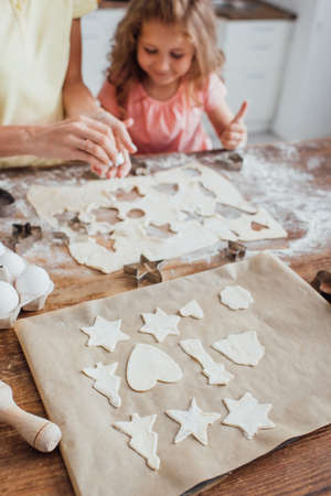selective focus of raw multi-shaped cookies on baking paper near mom and daughterの写真素材