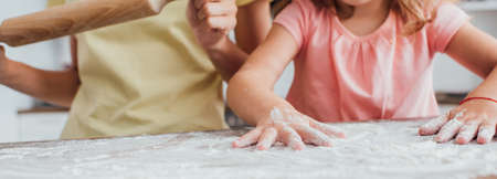 partial view of daughter scattering flour on kitchen table near mother holding rolling pin, panoramic shotの写真素材