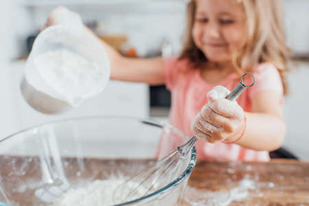 selective focus of girl pouring flour into glass bowl while holding whiskの写真素材