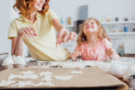 selective focus of raw multi-shaped cookies on baking paper near mother and daughterの写真素材