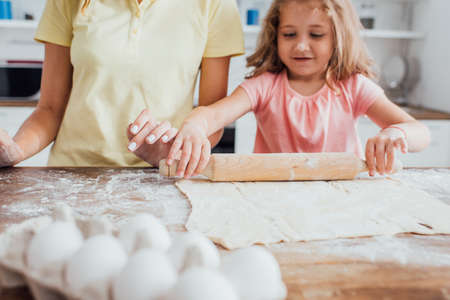 cropped view of mother near daughter rolling out dough on table scattered with flourの写真素材