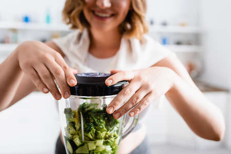 cropped view of woman touching blender with green lettuce and cucumberの写真素材