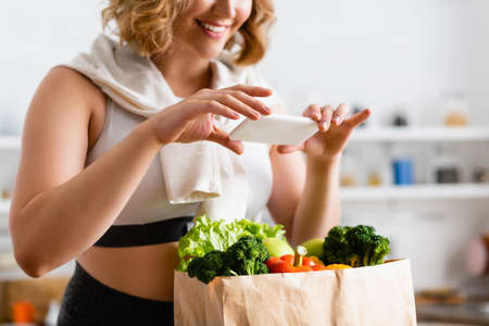 cropped view of woman taking photo of groceries in paper bag