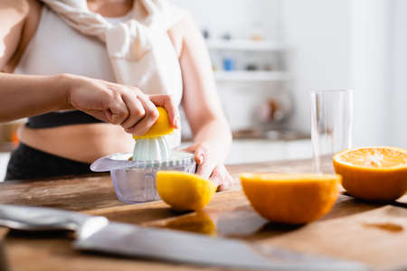 cropped view of woman holding half of orange near juicer while squeezing fruitの写真素材