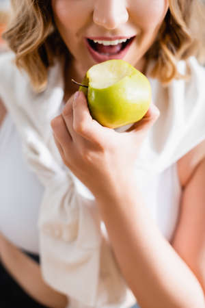 cropped view of young woman eating green appleの写真素材