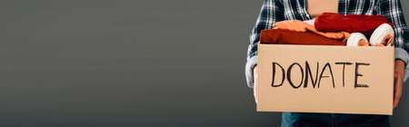 cropped view of woman holding box with donate lettering and clothes on gray background, panoramic shotの写真素材