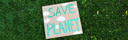 Horizontal crop of placard with save planet lettering on green grass, ecology concept