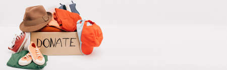 panoramic shot of cardboard box with donated accessories, clothes and footwear isolated on white,...
