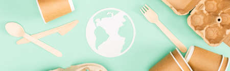 Panoramic shot of disposable tableware and paper earth sign on green background, ecology conceptの写真素材