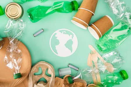 Top view of plastic bottles, accumulators and disposable tableware near paper earth sign on green...