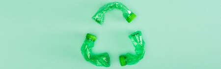 Panoramic shot of recycle sign from crumpled plastic bottles on green background, ecology concept