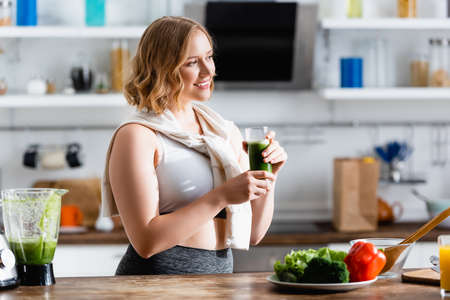 young woman holding glass of green smoothie and looking awayの写真素材