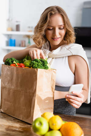 selective focus of woman taking selfie with groceries in paper bagの写真素材
