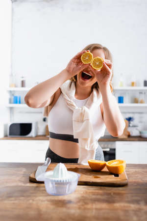 selective focus of woman covering eyes with halves of oranges near juicerの写真素材