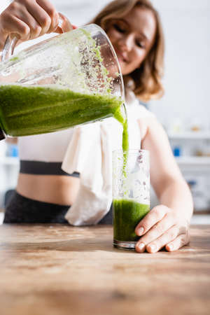 selective focus of woman pouring green smoothie in glassの写真素材