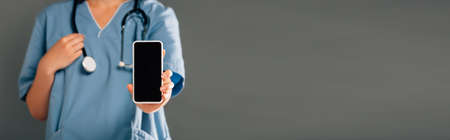 cropped view of doctor with stereoscope holding smartphone and blank screen isolated on gray,...