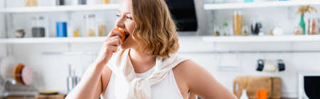 panoramic crop of woman eating fresh peach in kitchenの写真素材