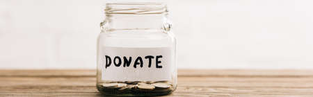 penny jar with donate lettering on wooden surface on white background, panoramic shot