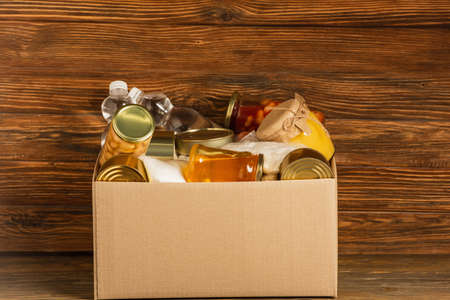 cardboard box with donated food on wooden background, charity concept