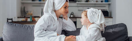 daughter and mother talking while sitting on sofa in bathrobes and towels on heads, panoramic shotの写真素材