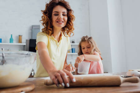 selective focus of mother taking rolling pin near daughter holding measuring jugの写真素材