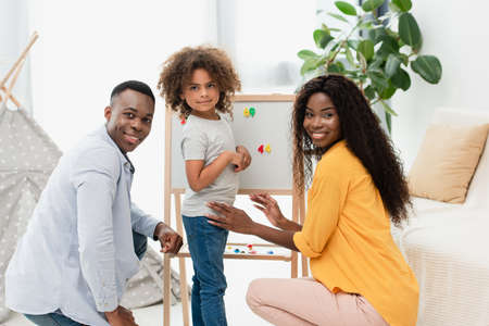 african american family looking at camera near magnetic easel