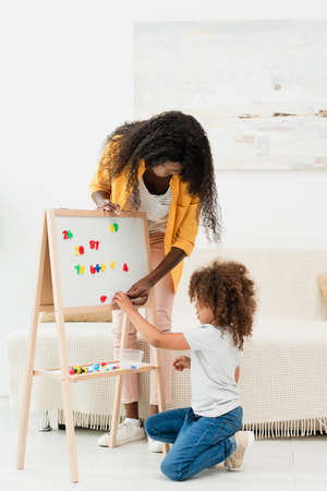 african american mother and curly daughter touching magnets on whiteboardの写真素材