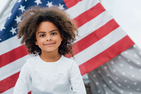 curly african american kid looking at camera near flag of americaの写真素材
