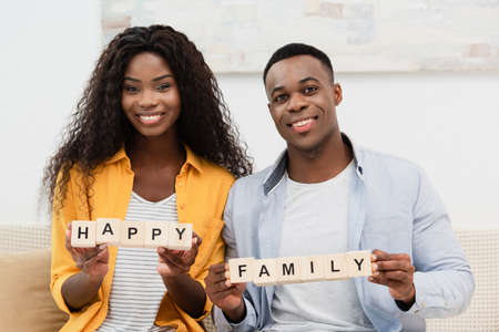 african american man and brunette woman holding wooden cubes with happy family lettering