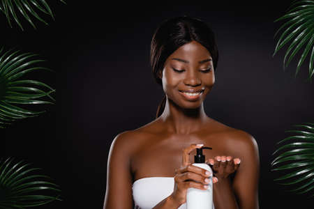 african american woman applying body lotion on hand near green palm leaves isolated on blackの写真素材