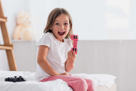 xcited girl showing joystick while sitting on bed in pajamas