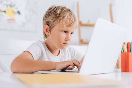 selective focus of concentrated boy in white t-shirt sitting at table and using laptop