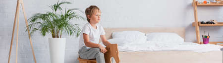 horizontal image of boy in pajamas riding rocking horse near potted plant and bedの写真素材